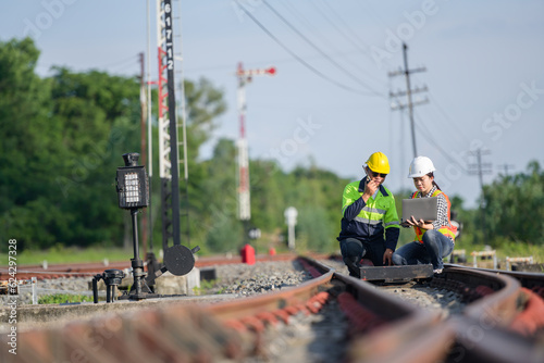 Asian railway worker or railway engineer maintaining railway track using laptop computer checking railway switch construction process and checking work in railway station.