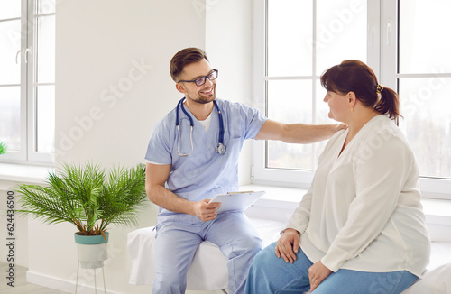 Overweight fat woman having consultation at the office. Portrait of friendly smiling doctor putting hand on shoulder supporting patient, giving consultation during medical examination in clinic.