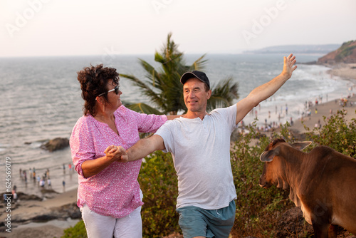 Happy tourist lifting arm up while female camper smiling, holding male hand. Mature couple spending vacation together.