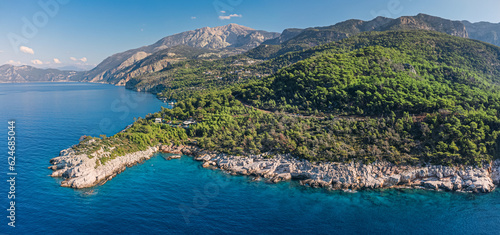 From high above, the Aegean Sea coast showcases its natural beauty, with rocky cliffs jutting out dramatically into the azure waters below.