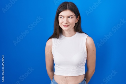 Young caucasian woman standing over blue background smiling looking to the side and staring away thinking.