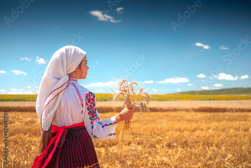 harvest time of golden wheat field and girl in traditional ethnic folklore costume with Bulgarian embroidery working on a meadow
