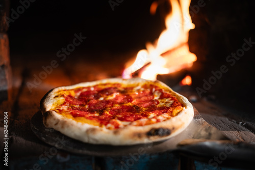 Placing italian pizza pepperoni in a wood-fired oven. Pizza with salami on pizza shovel in hot oven close up. Food photography