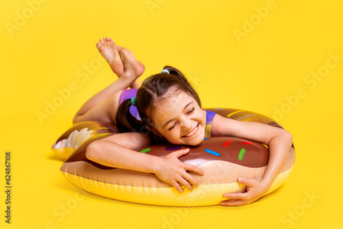 Cute little girl in swimsuit with inflatable ring on yellow background. Summertime kids activity content