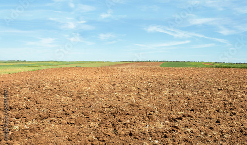 Freshly plowed farmland. The farmland is all moved and furrowed. It is ready to be sown with seeds. It is a sunny day with few clouds blue sky.