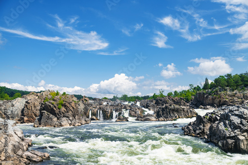 View of the Falls of the Potomac River in Virginia. A stormy stream of water among the rocks under the blue sky.