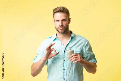 man hold cologne isolated on yellow, ok. man hold cologne in studio background.