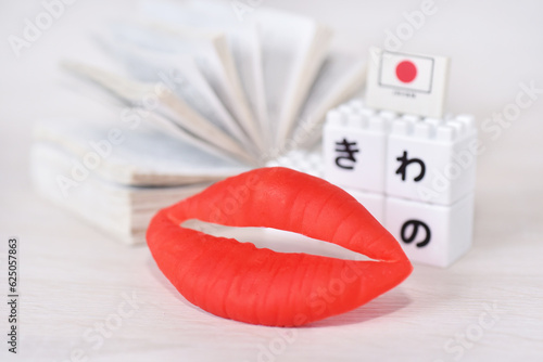 Red lip infront of the Japanese alphabet and opened book .Speaking Japanese fluently are advantages such as can connect to the new people, new bussiness, make more money and Immigration Benefits.