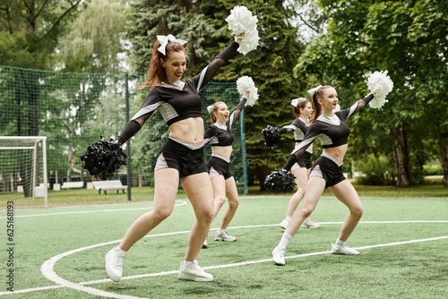 Young cheerleading girls dancing with pompom on football fieild outdoors
