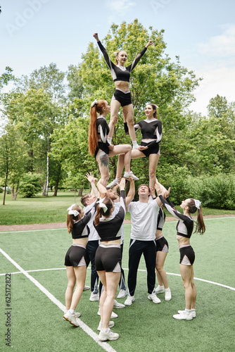 Vertical image of team of cheerleading training together with coach outdoors