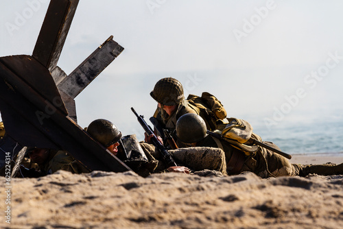 Historical reconstruction. An American infantry soldiers from the World War II fighting on the beach between smoke and dust.