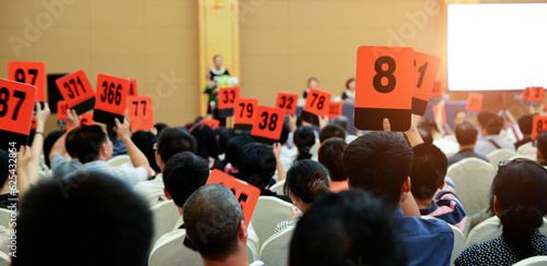 Crowd of bidders holding their numbered bidding paddles at an auction