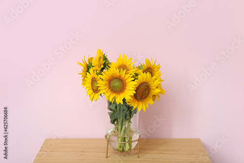 Vase with sunflowers on table near pink wall