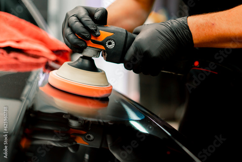 Close-up of a car wash worker using a polishing machine to polish the hood of a black luxury car 