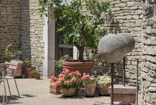 Cozy courtyard of a French house, a table with chairs on an open terrace with pot flowers. Outdoor cafe in summer in Provence, France, Europe. Ancient stone building.