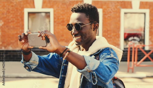 Portrait of happy smiling young african american man taking selfie with phone on city street