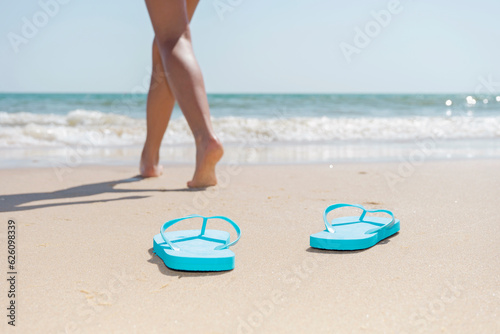 A bather woman's legs on the beach walking from her flip flops into the sea. Enjoying summer vacations.