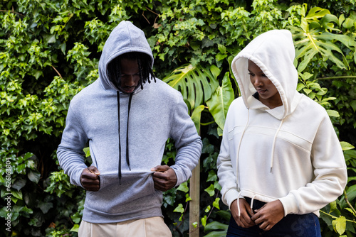 African american couple wearing white and grey hooded sweatshirts in garden