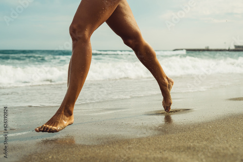 beautiful tanned female legs walk on the sand against the backdrop of the sea on the beach on a sunny day