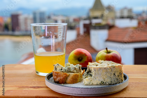 Food pairing in Asturias, blue cow cabrales cheese from Arenas served outdoor with glass of natural apple cider and view on San Lorenzo beach in Gijon