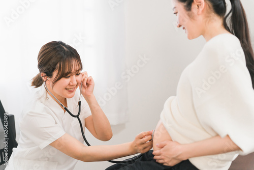 産婦人科・婦人科の病院で胎児の心音・胎動を聴診器で診察する女性医師・医者と妊婦の妊婦女性（妊婦健診） 