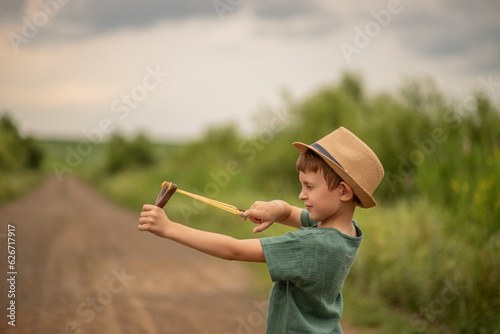 child boy of primary school age holds a slingshot in his hands plays and squinted his eye