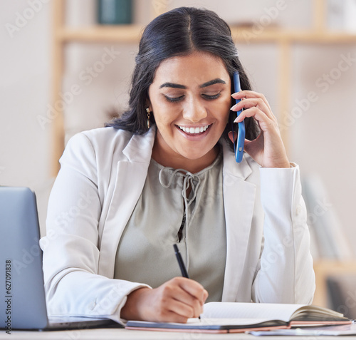Business woman, phone call and writing in office for networking, schedule and communication. Happy indian female worker talking on smartphone, planning agenda and calendar administration in notebook