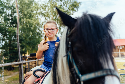 Portrait of little cute girl with two braids walking with a pony in manege at open air outdoor. Human and horse friendship, hippotherapy and recreation concept.