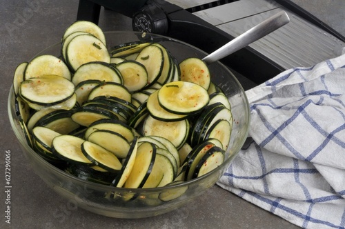 Rondelles de courgettes crues dans un saladier de marinade avec une mandoline de cuisine et un torchon