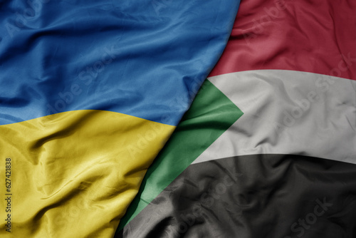big waving national colorful flag of ukraine and national flag of sudan .