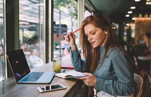 Focused woman sitting with notebook and pen in cafe