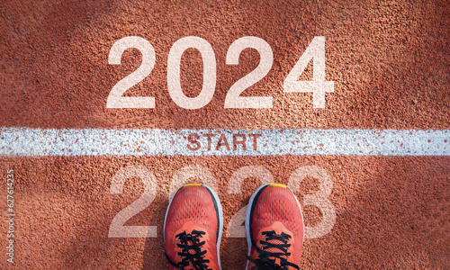 New year 2024 concept, beginning of success. Text 2024 written on asphalt road and male runner preparing for the new year. Concept of challenge or career path and change.