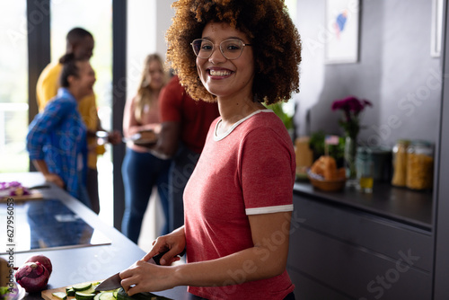 Portrait of happy biracial woman cutting vegetables with diverse friends in kitchen