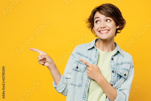 Young happy woman she wear green t-shirt denim shirt casual clothes point index finger aside indicate on workspace area copy space mock up isolated on plain yellow background studio Lifestyle concept