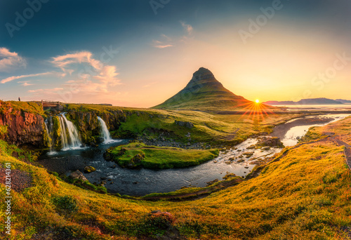 Sunrise over volcanic Kirkjufell mountain with waterfall flowing in summer at Iceland