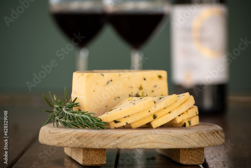 Queso manchego con epazote sobre una tabla de madera y copas de vino al fondo delicioso aperitivo