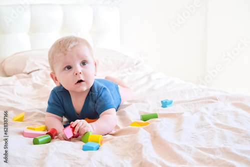 baby boy in blue bodysuit playing with colorful wooden eco toys on bed