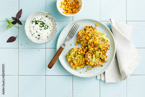 Zucchini and corn fritters with sour cream and herbs. Top view, flat lay.