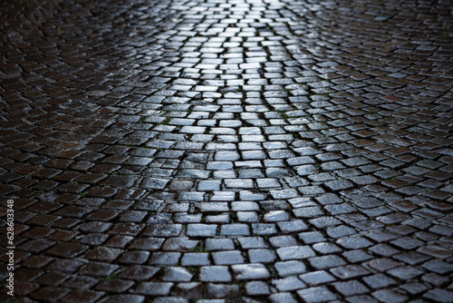 Cobblestone in a narrow street in Stresa, Italy. Wet shiny historic basalt ashlars or blocks reflecting blue sky and sunshine after rain. Old pavement background with typical surface and structure.