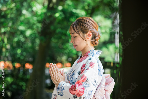 神社で手を合わせて参拝をする浴衣姿の女性