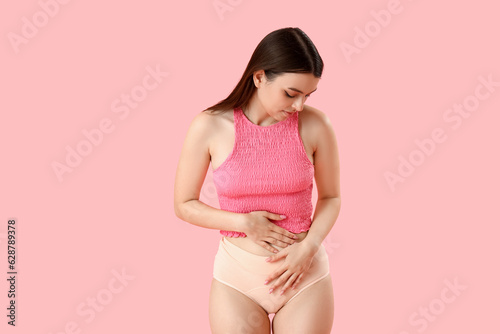 Young woman having menstrual cramps on pink background