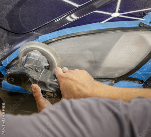 Man making headlight clean with polishing machine selective focus. Close-up. Master repairman polishing headlights of car in workshop using machine closeup. 