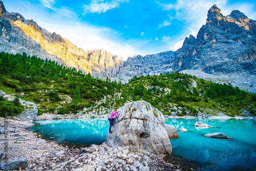 Athletic woman climbing down from big boulder at turquoise Sorapis lake with dito di dio in the evening. Lake Sorapis, Dolomites, Belluno, Italy, Europe.