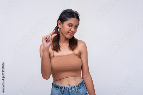 A young asian woman expressing something tiny or little with her thumb and index finger, looking unimpressed or condescending. Describing a small package. Isolated on a white background.