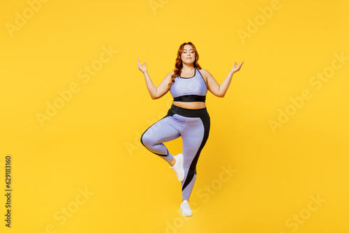Full body young chubby plus size big fat fit woman wear blue top warm up train raise up hands leg in yoga om gesture meditate isolated on plain yellow background studio home gym Workout sport concept
