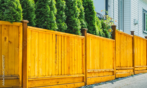 Beautiful new wooden fence around the house. Wooden fence with wooden gate with green lawn.