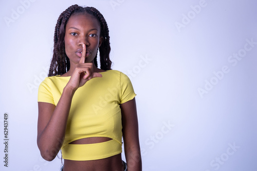 Shh, ¡cállate! Bonita chica de color mirando a la cámara, pidiendo silencio secreto con el dedo en los labios, conversación confidencial. tiro del estudio aislado fondo blanco