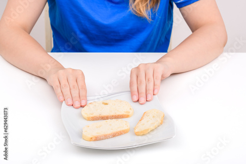 Kromka bialego pieczywa na talerzu, dziewczyna z niechęcią odsuwa od siebie talerz 