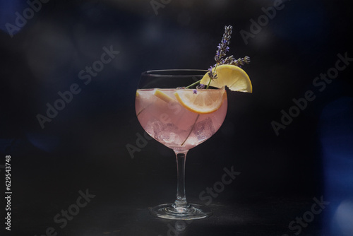 Fancy cocktail with fresh fruit. Gin and tonic drink with ice at a party, on a black background. Alcohol with lavender and lemon, toned image