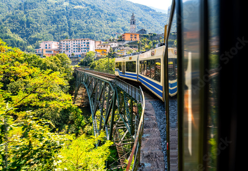 View out of a coach of the Centovalli railway, a popular narrow gauge train connecting Locarno Switzerland and Domodossola Italy. Passing a historic steel construction valley bridge in Intragna.